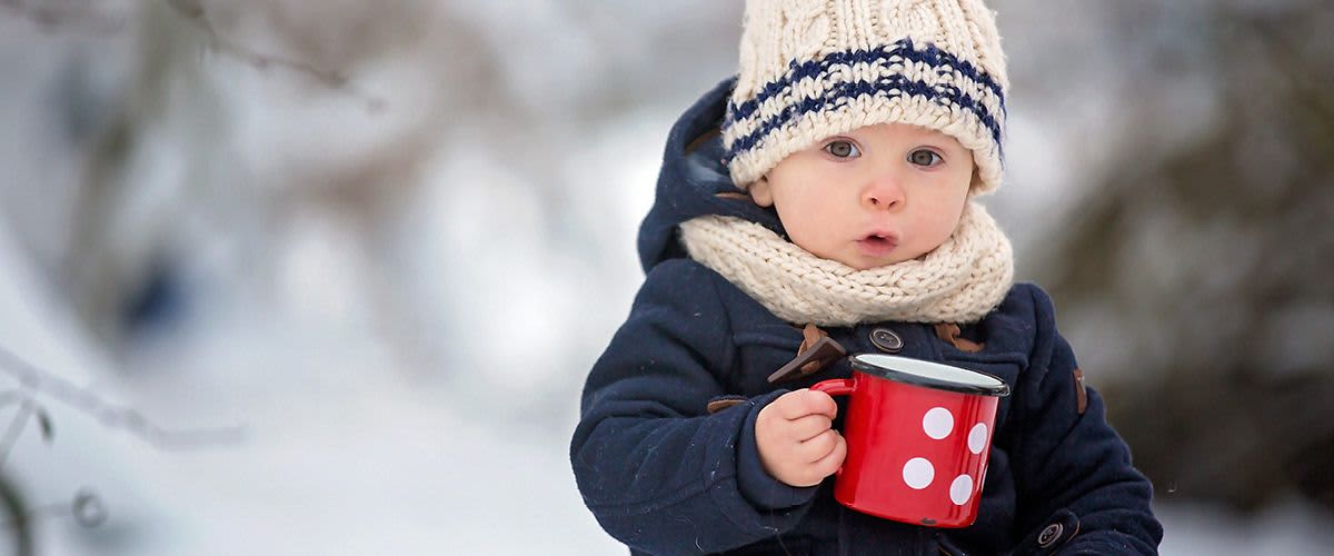 Dítě v zimním oblečení držící červený hrnek s puntíky
