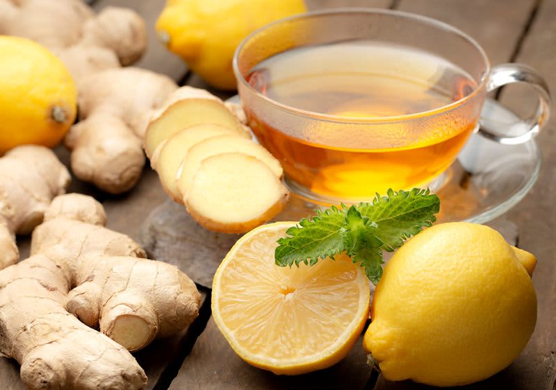 Čaj s citronem a zázvorem na dřevěném stole, obklopený čerstvými citrony a zázvorem.