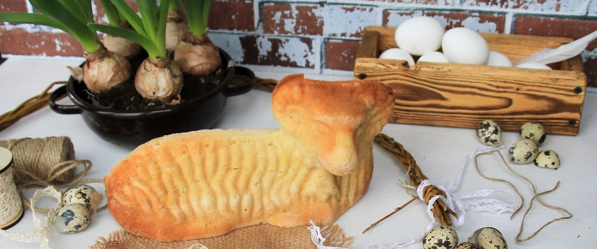 Velikonoční beránek, květiny, vejce a dekorace na stole před cihlovou zdí