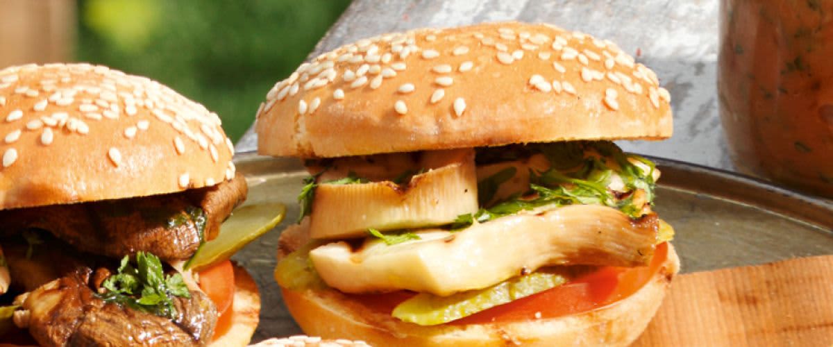 Hamburgery s houbami a sýrem, plátky okurek na dřevěném prkénku