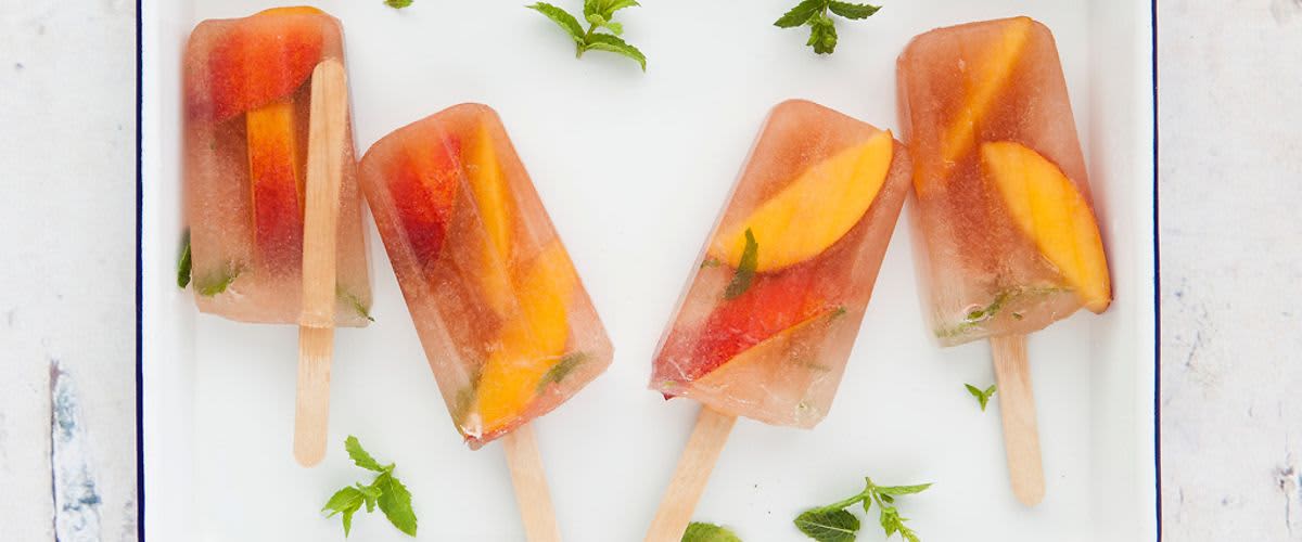 Ovocné nanuky s plátky broskví a lístky máty na bílém podnosu