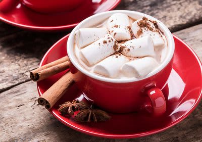 Horká čokoláda s marshmallows v červeném hrnku na dřevěném stole s kořením.