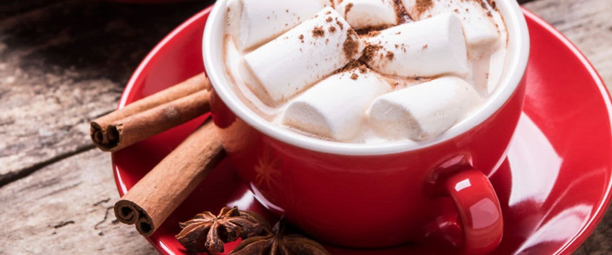 Horká čokoláda s marshmallows v červeném hrnku na dřevěném stole s kořením.