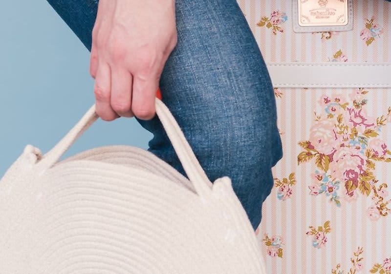 Ruka držící bílou kabelku vedle květinového kufru a modrých džínů