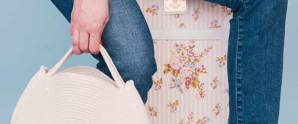 Ruka držící bílou kabelku vedle květinového kufru a modrých džínů