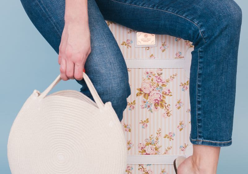 Osoba sedící na květinovém kufru drží bílou kulatou kabelku