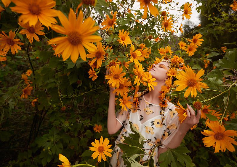 Žena obklopená velkými oranžovými květy v přírodě