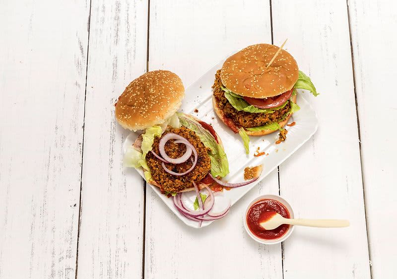 Dva hamburgery na talíři s miskou kečupu na bílém dřevěném stole.