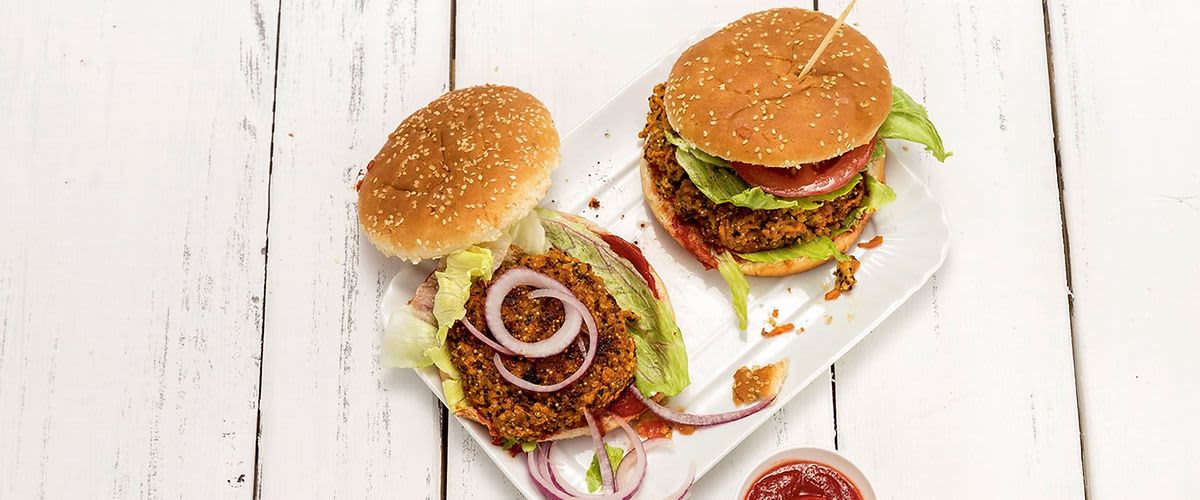 Dva hamburgery na talíři s miskou kečupu na bílém dřevěném stole.