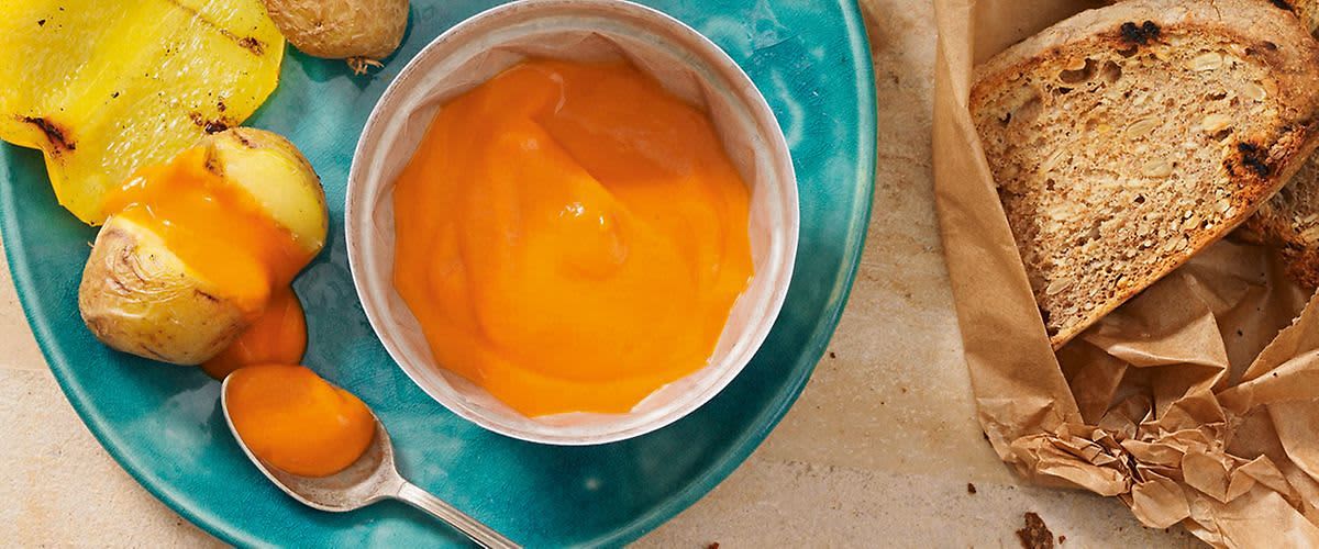 Talíř s omáčkou v misce, pečené brambory a lžička na modrém talíři