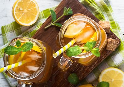 Ledový čaj s citronem a mátou ve sklenicích na dřevěném prkénku, obklopený citrony a kostkami cukru.
