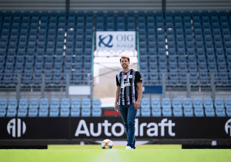 Fotbalista stojící na hřišti před prázdnými tribunami stadionu