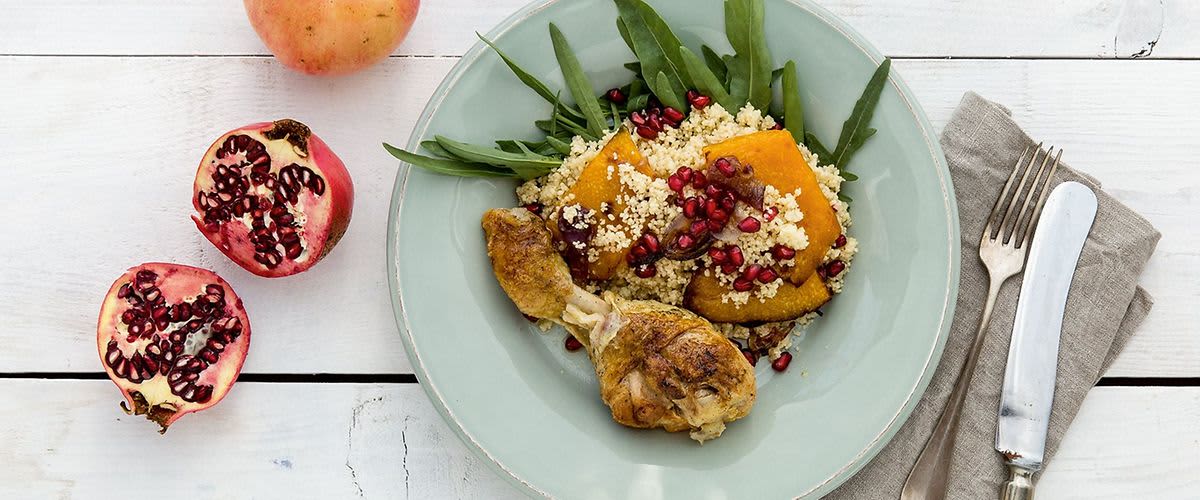 Talíř s pečeným kuřetem, kuskusem, dýní a granátovým jablkem na dřevěném stole