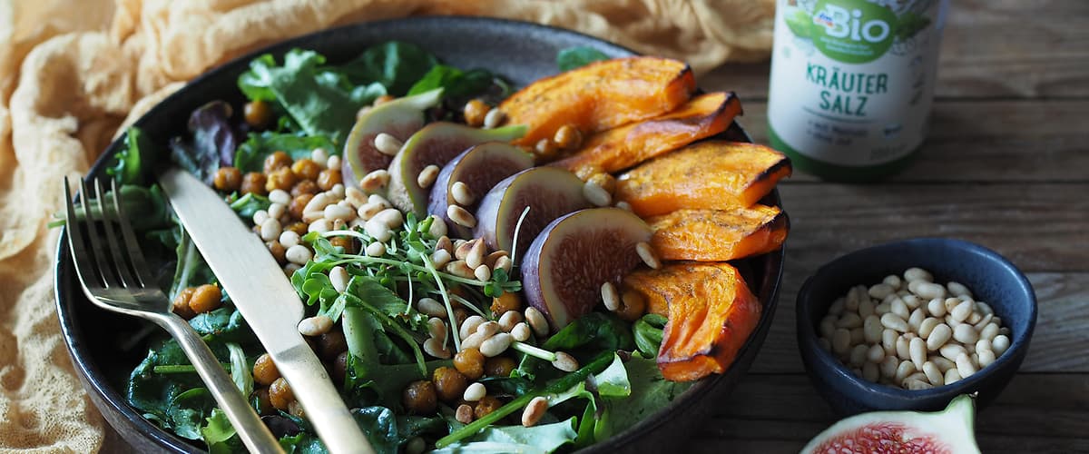 Salát s pečenou dýní, fíky, piniovými oříšky a cizrnou na dřevěném stole s příborem a kořením