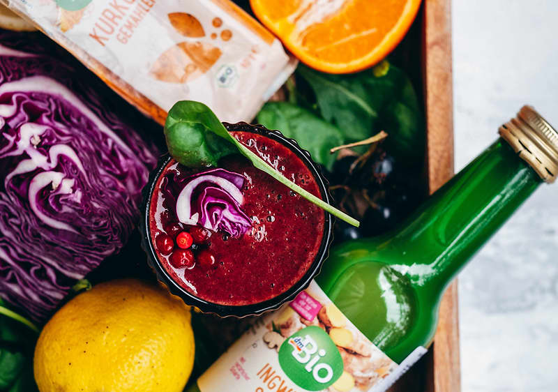 Smoothie s červeným zelím, citronem, pomerančem, špenátem a bio zázvorovým nápojem na dřevěném podnosu