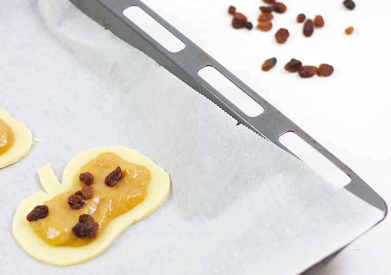 Pečicí plech s těstem, jablečnou náplní a rozinkami, vedle rozinky na stole