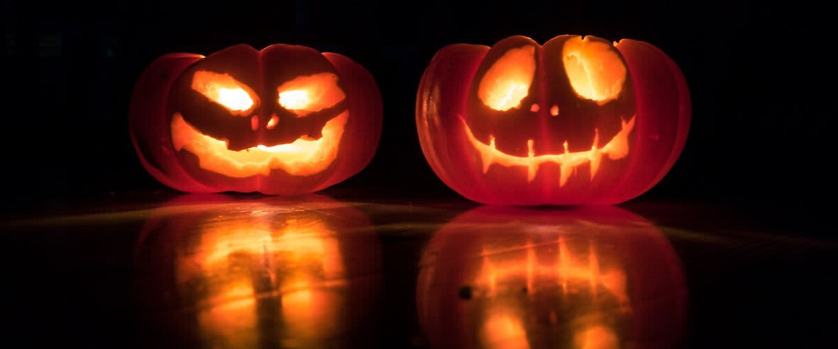 Dvě vyřezané dýně s rozsvícenými strašidelnými obličeji na tmavém pozadí