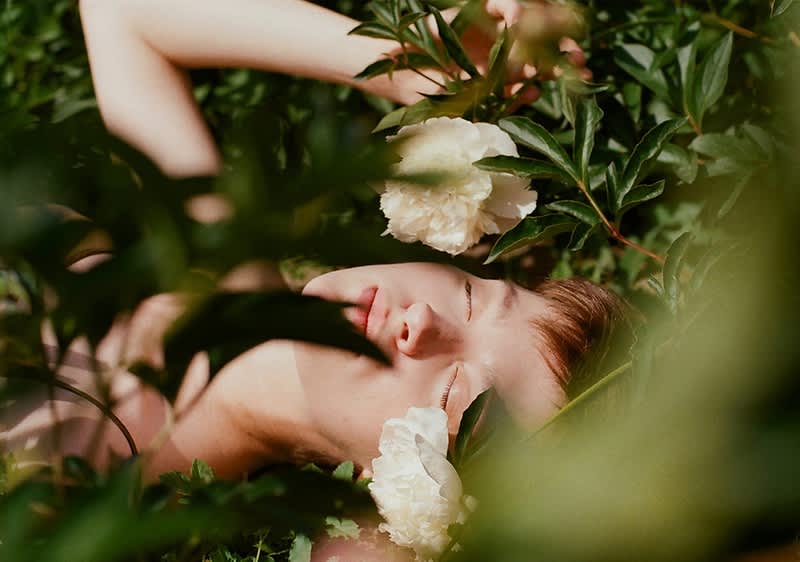 Žena ležící v trávě obklopená bílými květy