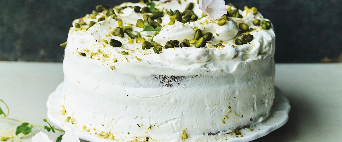 Dort s bílým krémem, posypaný pistáciemi a ozdobený květinami na bílém talíři.