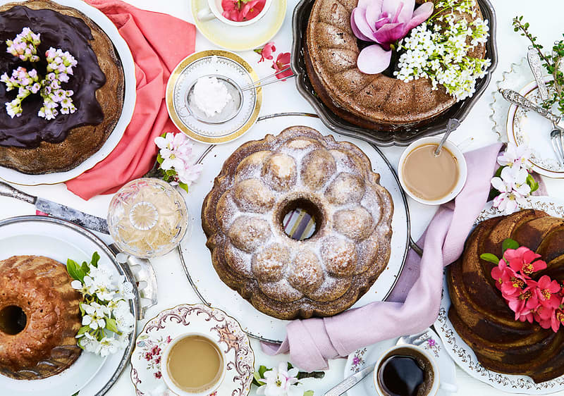 Různé druhy bábovek na stole s květinami a šálky kávy