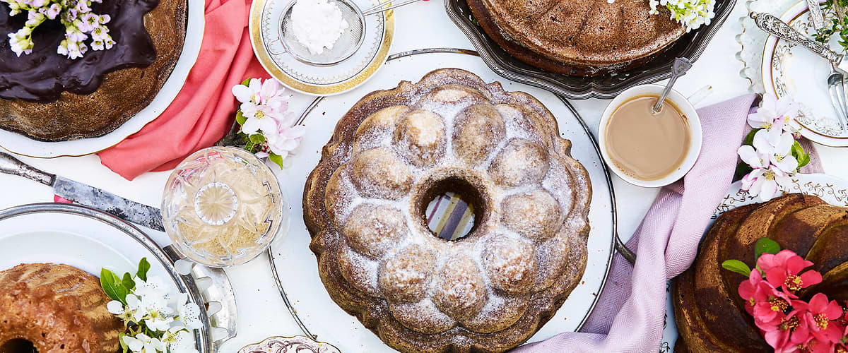 Různé druhy bábovek na stole s květinami a šálky kávy