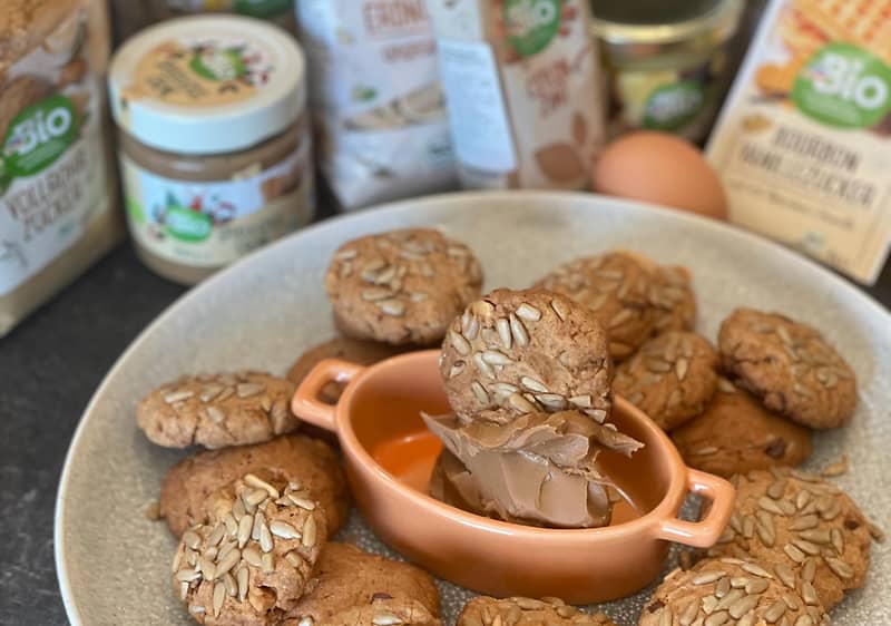 Sušenky s oříšky na talíři, obklopené ingrediencemi jako ořechové máslo a vejce