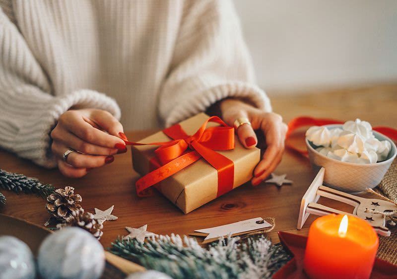 Žena balí dárek s červenou stuhou