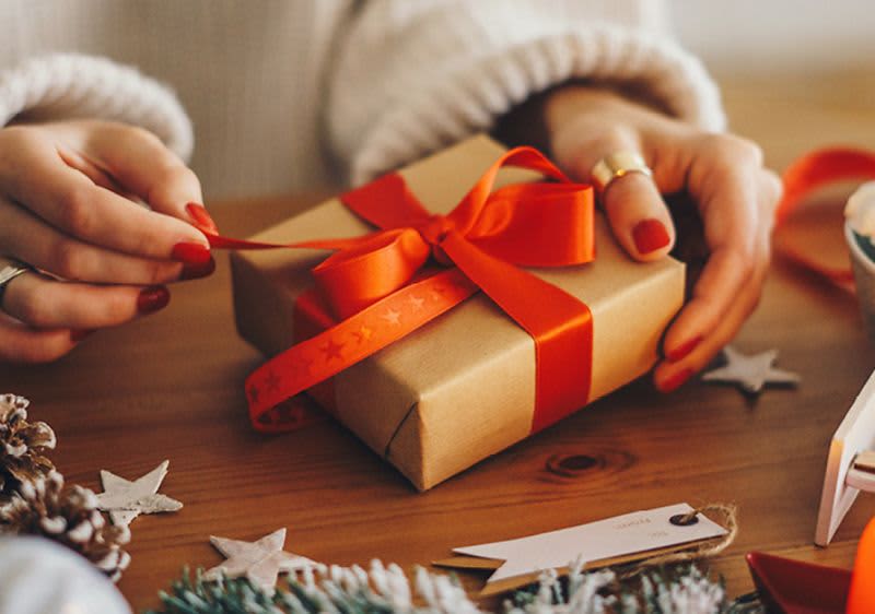 Žena balí dárek s červenou stuhou