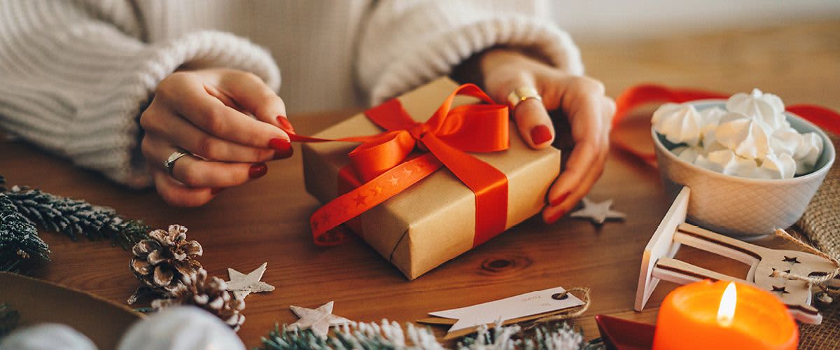 Žena balí dárek s červenou stuhou
