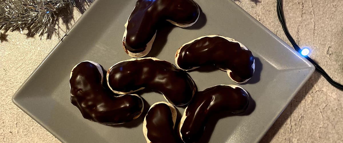 Čokoládové cukroví na šedém talíři, vánoční dekorace a světýlka na pozadí