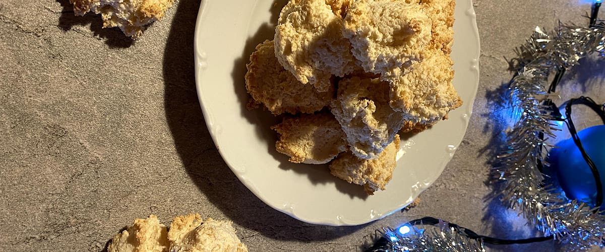 Kokosové sušenky na talíři, vánoční ozdoby a stříbrný řetěz na stole