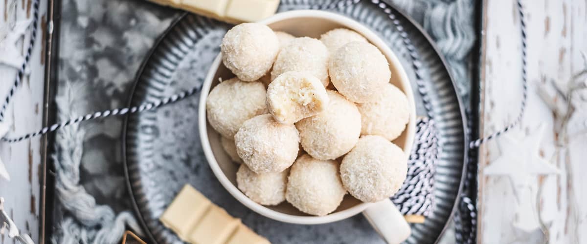 Kokosové kuličky v hrnku s bílou čokoládou na podnosu s vánočními dekoracemi