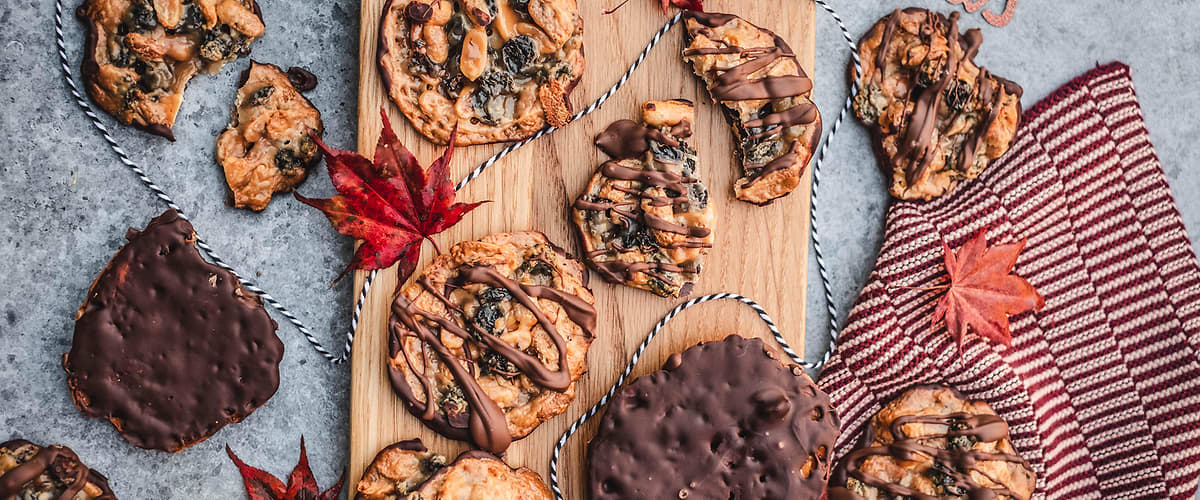 Vánoční sušenky na dřevěném prkénku, některé s čokoládou, ozdobené podzimními listy a textem Merry Christmas
