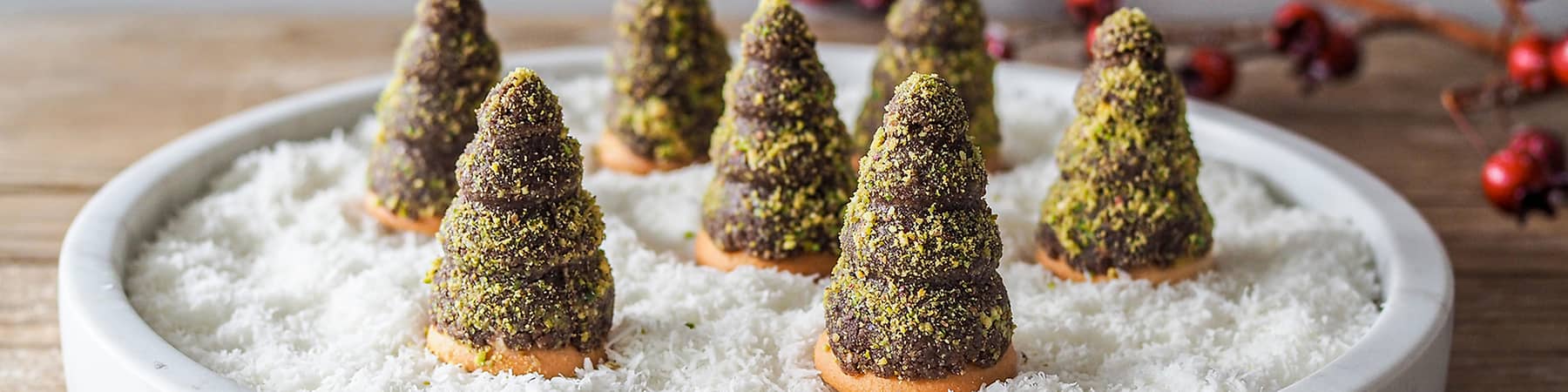 Čokoládové stromečky na talíři s kokosovým sněhem, dekorace s červenými bobulemi v pozadí