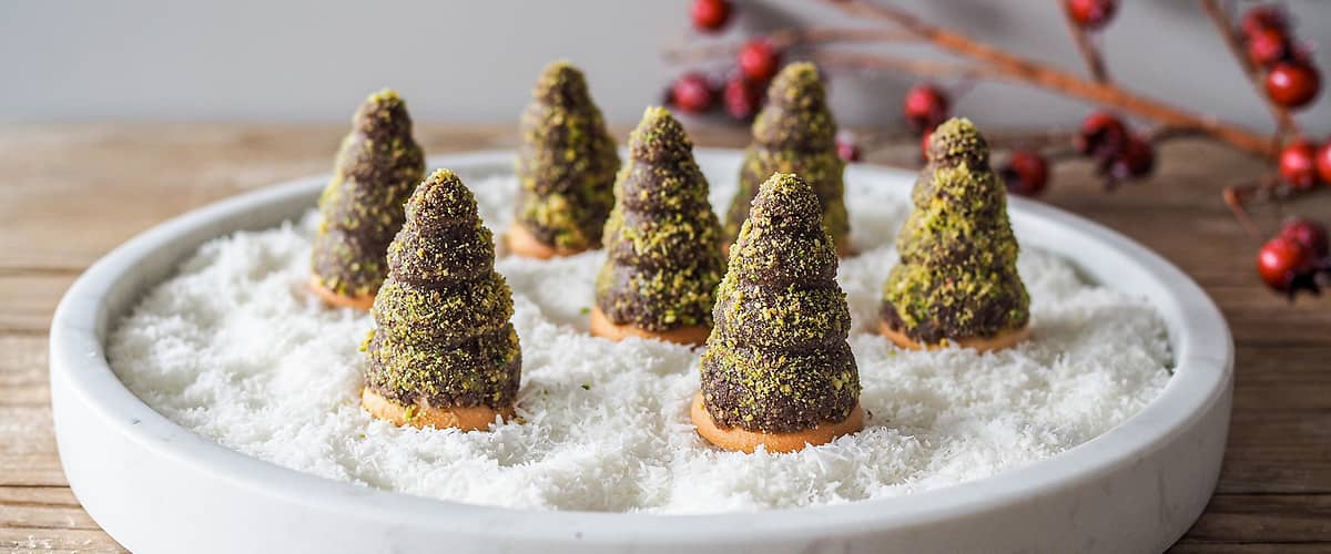 Čokoládové stromečky na talíři s kokosovým sněhem, dekorace s červenými bobulemi v pozadí