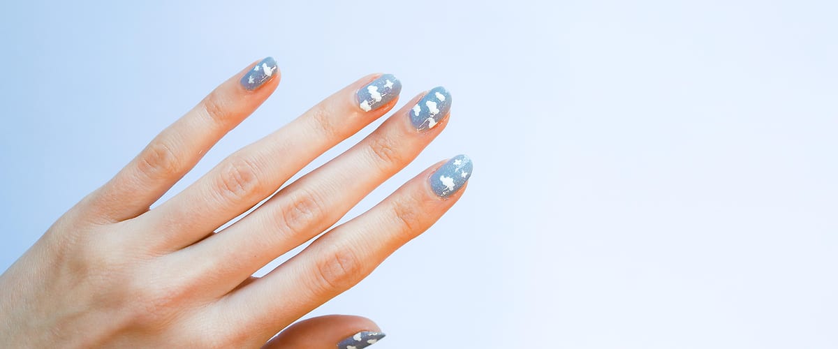 Ruka s modrými nehty a bílými vzory na světlém pozadí