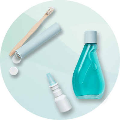 Eine blaue Mundspülungsflasche, ein Nasenspray, ein Zahnpflege-Set mit Bambuszahnbürste und zwei Tabletten auf hellem Hintergrund