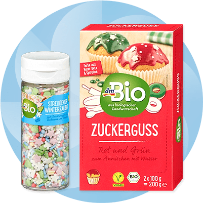 Eine rote Verpackung mit der Aufschrift „Zuckerguss Rot und Grün zum Anrühren mit Wasser“ neben einer weißen Dose mit der Aufschrift „Streudekor Winterzauber“ und bunten Streuseln