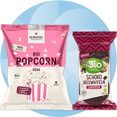 Eine rosa Verpackung mit der Aufschrift „Heimatgut Bio Popcorn süß“ und eine braune Verpackung „dmBio Schoko Reiswaffeln Zartbitter“