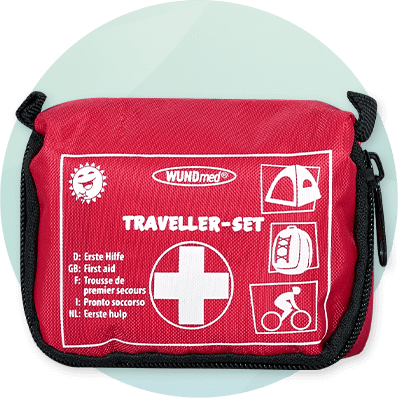 Rotes Reise-Erste-Hilfe-Set mit weißem Kreuz, Aufschrift „TRAVELLER-SET“ und Icons für Zelt, Rucksack und Fahrrad, Herstellername „WUNDmed“