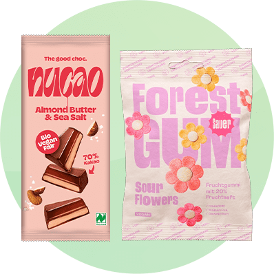 Links eine rosa Schokoladenverpackung mit der Aufschrift „nucao Almond Butter & Sea Salt“, rechts eine bunte Fruchtgummiverpackung mit „Forest Gum Sour Flowers“
