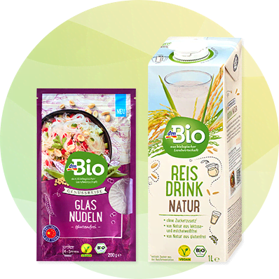Eine violette Verpackung mit der Aufschrift „dmBio Glasnudeln“ neben einer Kartonverpackung „dmBio Reis Drink Natur“
