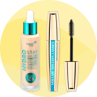 Drei Kosmetikprodukte vor gelbem Kreis: links flüssige Foundation „Hydro Stay Silky Serum Foundation“ mit Pipette und Aufschrift „12H“, Mitte goldblaue Mascara „Volume Million Lashes Waterproof“, rechts geöffneter Mascara-Applikator ohne Verpackung