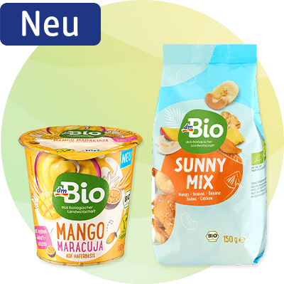 Zwei dmBio-Produkte vor hellem Kreis: links gelbe Tüte „Knusperecken Mais & Hülsenfrüchte 80 g“ mit dmBio-Logo und Snackabbildung, rechts grüner Tetrapak „Eistee mit Matcha & Yuzu 0,5 l“ mit dmBio-Logo und Zitronenscheibenlabel