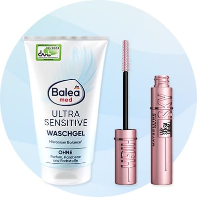 Links eine weiße Tube Balea med Ultra Sensitive Waschgel mit blauer Grafik und dem Hinweis „Ohne Parfum, Parabene und Farbstoffe“, rechts eine offene roségoldene Mascara von Maybelline mit Bürstchen nebeneinander, vor hellem kreisförmigem Hintergrund