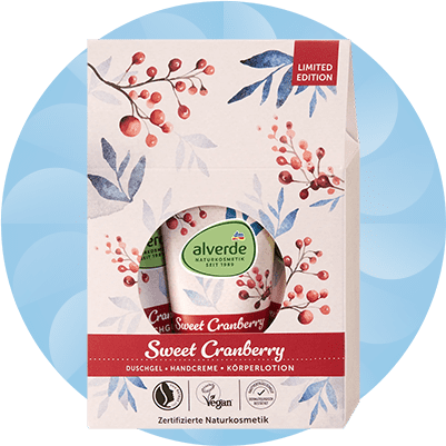 Geschenkset in pastellrosa Verpackung mit Aquarell-Zweigen und roten Beeren, Sichtfenster zeigt grüne alverde-Deckel; Aufschrift „Sweet Cranberry“, rotes Band mit Produktangaben „Duschgel · Handcreme · Körperlotion“ und „Limited Edition“