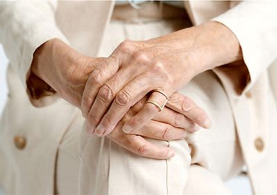 Ältere Hände mit Ring auf beige Kleidung