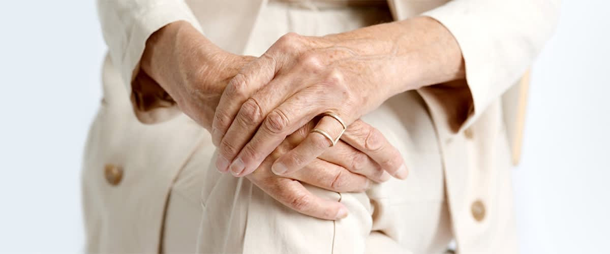 Ältere Hände mit Ring auf beige Kleidung