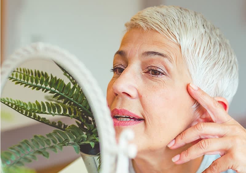 Aeltere Frau betrachtet ihr Gesicht im Kosmetikspiegel