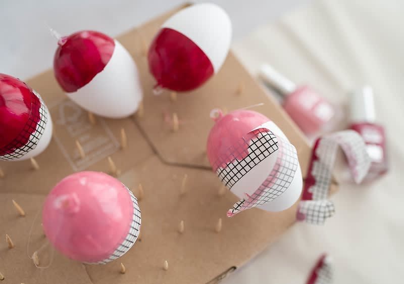 Weiße Ostereier werden mit rotem und rosa Nagellack bemalt und trocknen auf einem Karton mit Holzstäben.
